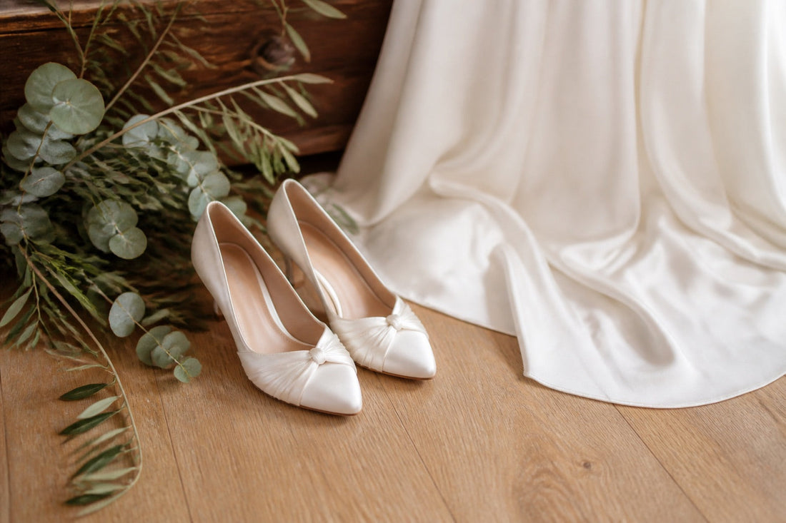Chaussures de mariée en satin ivoire posées près d'une robe blanche, lumière naturelle douce