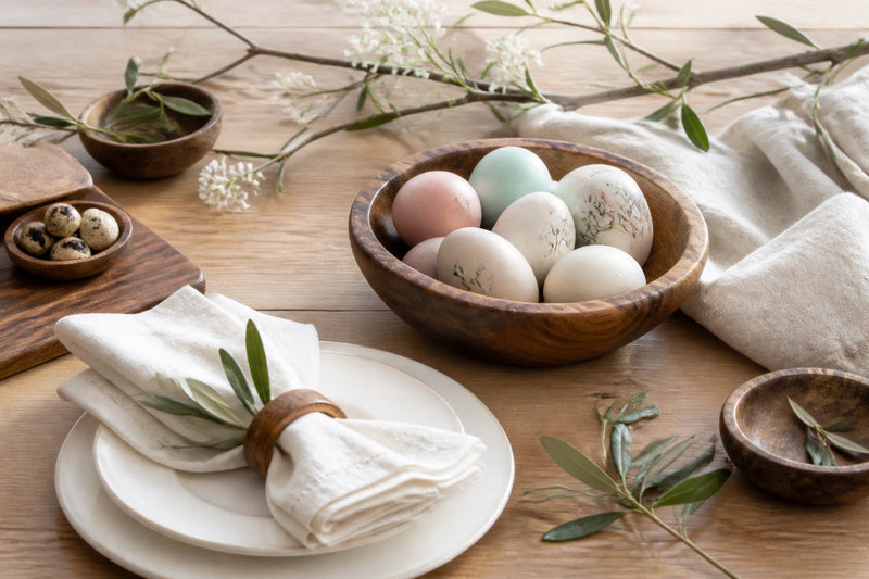 Décoration de table de Pâques champêtre avec œufs pastel, branches fleuries et vaisselle en grès sur une table en bois clair